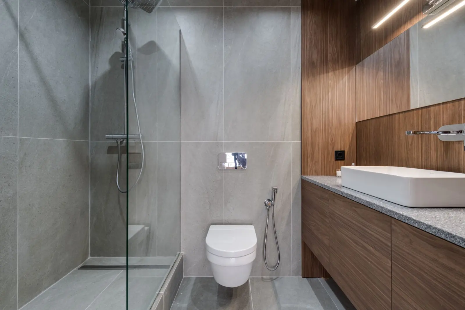 Modern walk-in glass shower in a small bathroom with wood vanity finish