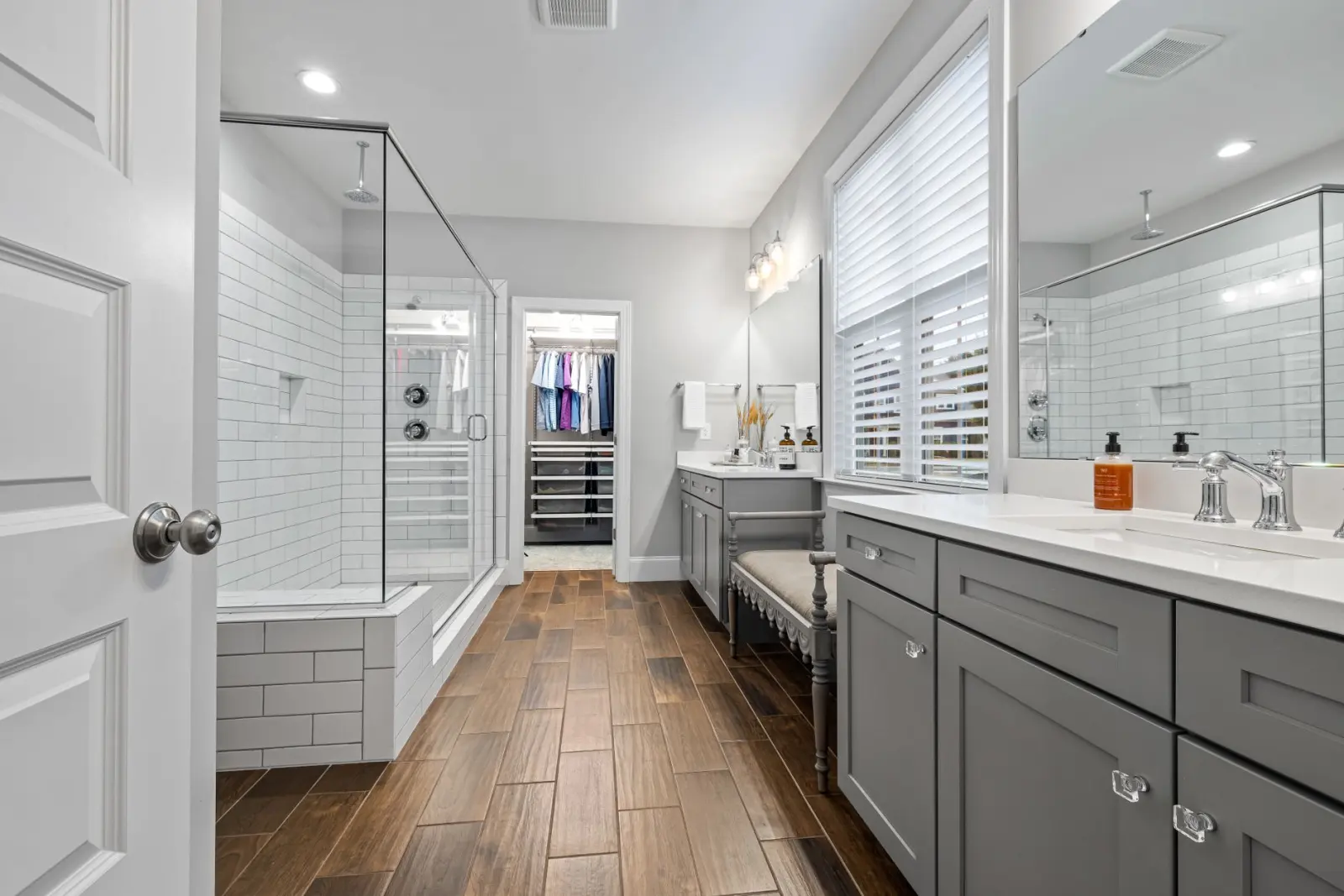 Modern bathroom with a glass-enclosed walk-in shower, wood flooring, and gray cabinetry